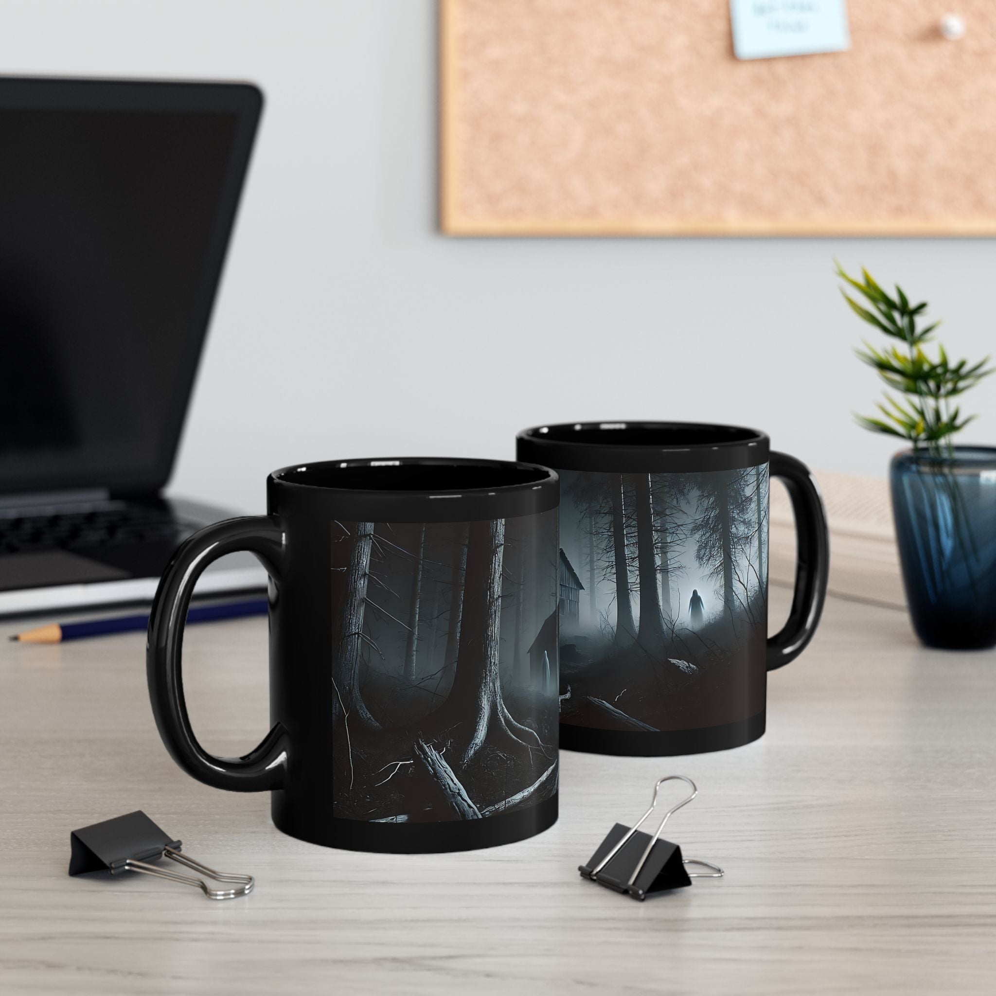 Two black mugs with forest design on a desk with office items.